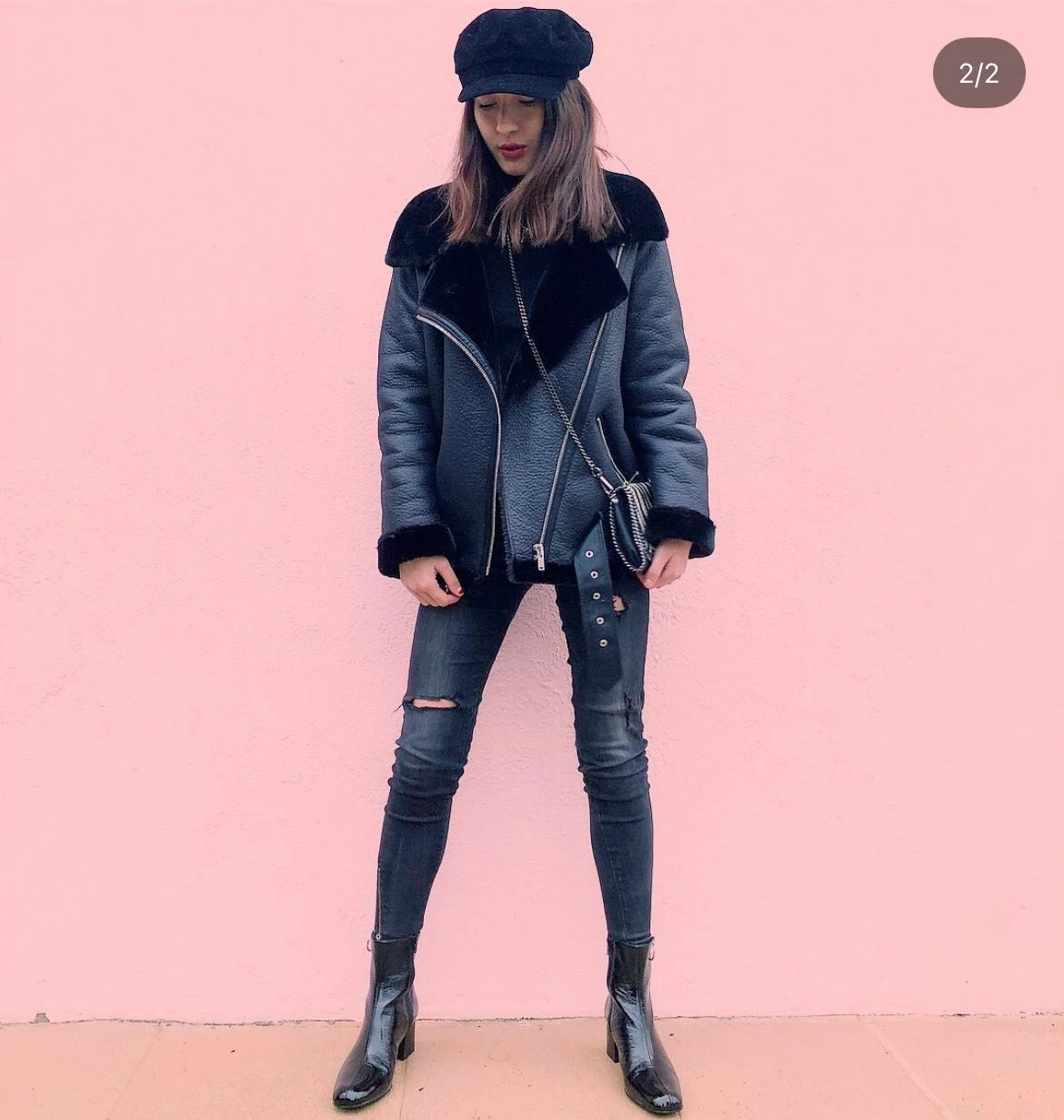 Saivaly en veste noire devant un mur rose